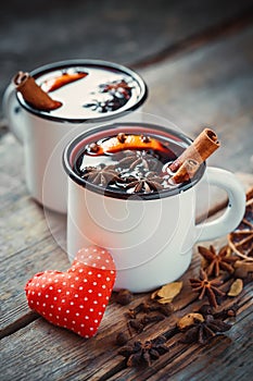 Mulled wine in rustic mugs with spices and red heart