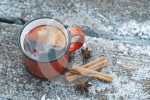 Mulled wine or tea on a wooden background during a snowfall in the forest. Winter hot drinks with aromatic spices of