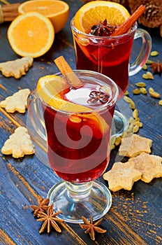 Mulled wine with various winter spices on the black wooden background decorated with Christmas cookies and fresh orange slices