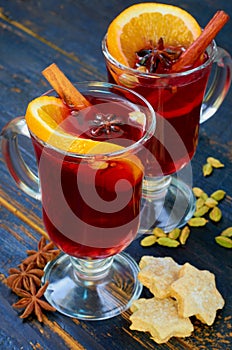 Mulled wine with various winter spices - cinnamon and anise stars on the black wooden background decorated with Christmas cookies