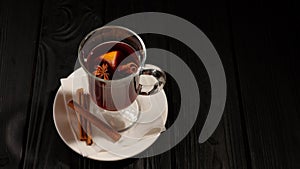 Mulled wine on white plate on black wooden table, cinnamon sticks and orange, top view