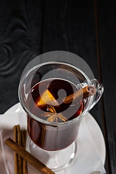 Mulled wine on white plate on black wooden table, cinnamon sticks and orange, top view