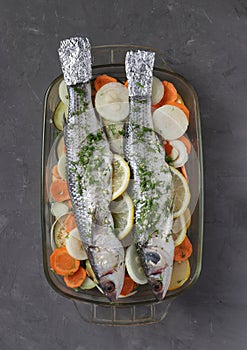 Mullet seasoned with lemon and spices is prepared for roasting together with vegetables in glass dish, vertical format