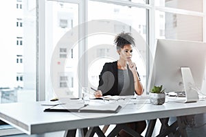 Mulling over her next business move. a young businesswoman using a computer at her desk in a modern office.