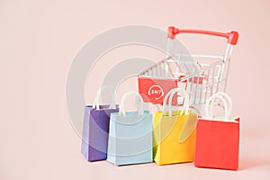 Multi color shopping bags and blurred shopping cart with 24 hours 7 days service sign on pink background