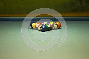 A multi-colored billiard balls lie on the blue cloth of the table in the pyramid of a triangle