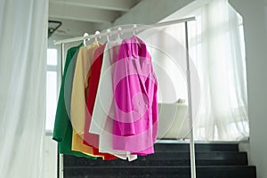Multi-colored bright jackets on a hanger against the background of the window