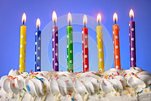 Multi-colored candles burn on a birthday cake on blue background