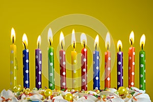 Multi-colored candles burn on a birthday cake on a yellow background