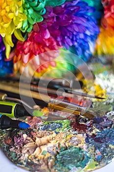 Multi-colored chrysanthemums on the palette with paints and brushes of the artist