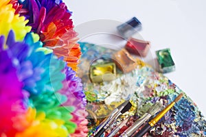 Multi-colored chrysanthemums on the palette with paints and brushes of the artist