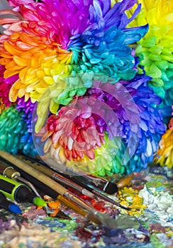 Multi-colored chrysanthemums on the palette with paints and brushes of the artist