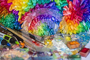 Multi-colored chrysanthemums on the palette with paints and brushes of the artist