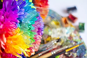 Multi-colored chrysanthemums on the palette with paints and brushes of the artist