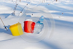 Multi-colored coffee cups and a plastic bottle stick out of the snow. Household waste environmental pollution concept