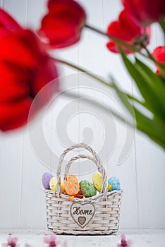Multi-colored Easter eggs in a basket on a white wooden background