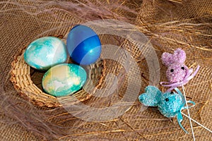 Multi-colored Easter eggs of blue tones and two Easter bunny on a stick on a brown cloth background. Close up