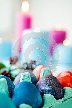 Multi-colored eggs lie in a tray, candles burn in the background. Easter holiday table, vertical