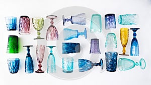 Multi-colored glass empty wine glasses and glasses lie on a white background. Beautiful vintage tableware made of multi-colored