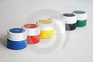 Multi-colored gouache stands in a row on a white textural background