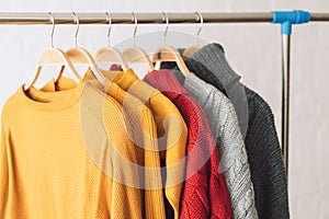 Multi-colored knitted sweaters on wooden hangers hang on an iron rack rale photo