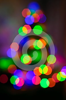 Multi-colored lights on the Christmas tree on dark background. The whole shot is defocused to use bokeh simulation