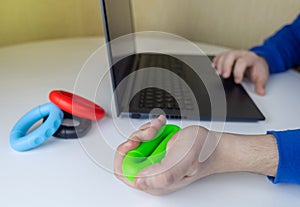 Hand gripper. Man squeezes rubber expander while working on his laptop. Concept of combining useful activity with necessary work.