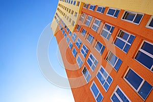 Multi-colored modern residential high-rise building with many glass windows standing against background of blue sky and