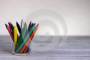 Multi-colored multicolored pencils in a transparent glass glass on a white wooden table