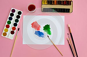 Multi-colored objects for drawing and creativity for children lie on a pink background. Bright watercolor paints, pencils, brushes