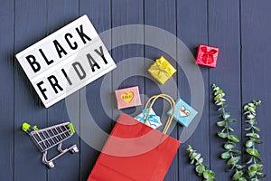 Multi colored packaging bags, trolley, sprig of eucalyptus, cup of coffee gift boxes lightbox with text Black Friday on  dark gray