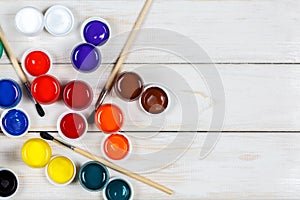 Multi-colored paint with brushes on a white wooden background