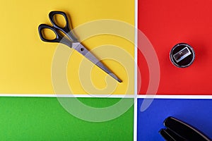 Multi-colored paper background. Yellow, green, red and blue. On the yellow background there are scissors, on the red sharpener, on