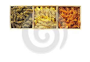 Multi-colored pasta in the form of spirals lie in wooden boxes that stand on a white table
