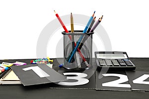 Multi-colored pencils notepad, book and pictures with numbers on a black table. Education concept.