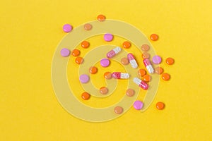 Multi-colored pills are scattered on a bright yellow background, top view. Medication for the disease for patients. Dose drugs and