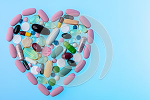 Multi-colored pills in the shape of heart on blue gradient background. Heart shape made of tablets, concept of treatment