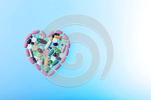 Multi-colored pills in the shape of heart on blue gradient background. Daily Vitamins dose. Heart shape made of tablets