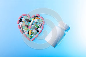 Multi-colored pills in the shape of heart and plastic jar on blue gradient background. Heart shape made of tablets