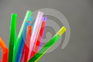 Multi colored plastic straws in a jar in front of a grey background