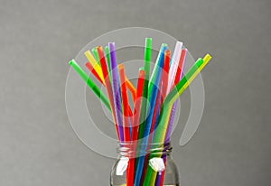 Multi colored plastic straws in a jar in front of a grey background