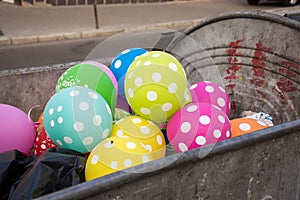 Multi-colored polka dot balloons are in the dumpster or garbage container and on one one sits fly. Party, celebration, fun, holida
