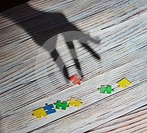 Multi-colored puzzles on a white wooden background, the shadow of a hand picks up one puzzle.concept of early childhood