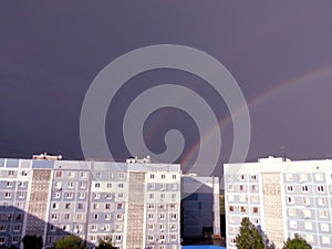 A multi-colored rainbow that creates a sky bridge against the background of rain clouds under the piercing rays of the summer sun.