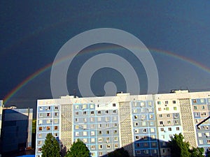 A multi-colored rainbow that creates a sky bridge against the background of rain clouds under the piercing rays of the summer sun.