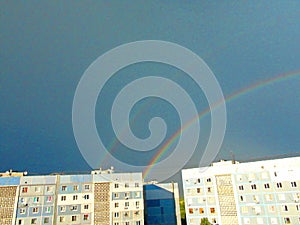 A multi-colored rainbow that creates a sky bridge against the background of rain clouds under the piercing rays of the summer sun.