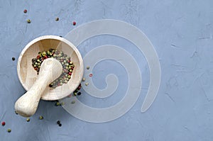 Multi-colored red green black peppercorns in a wooden mortar with pestle and scattered around on a ultimate gray