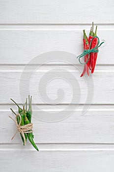 Multi-colored red and green hot chilli peppers tied with a scourge on a white wooden background or table with place for text
