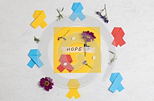 Multi-colored ribbons, flowers, the word hope and pills on stone.