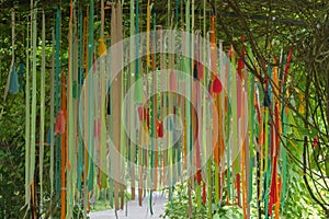 Multi-colored ribbons and ropes with knots of red, blue, yellow, green and orange hanging from arch covered with vines and foliage